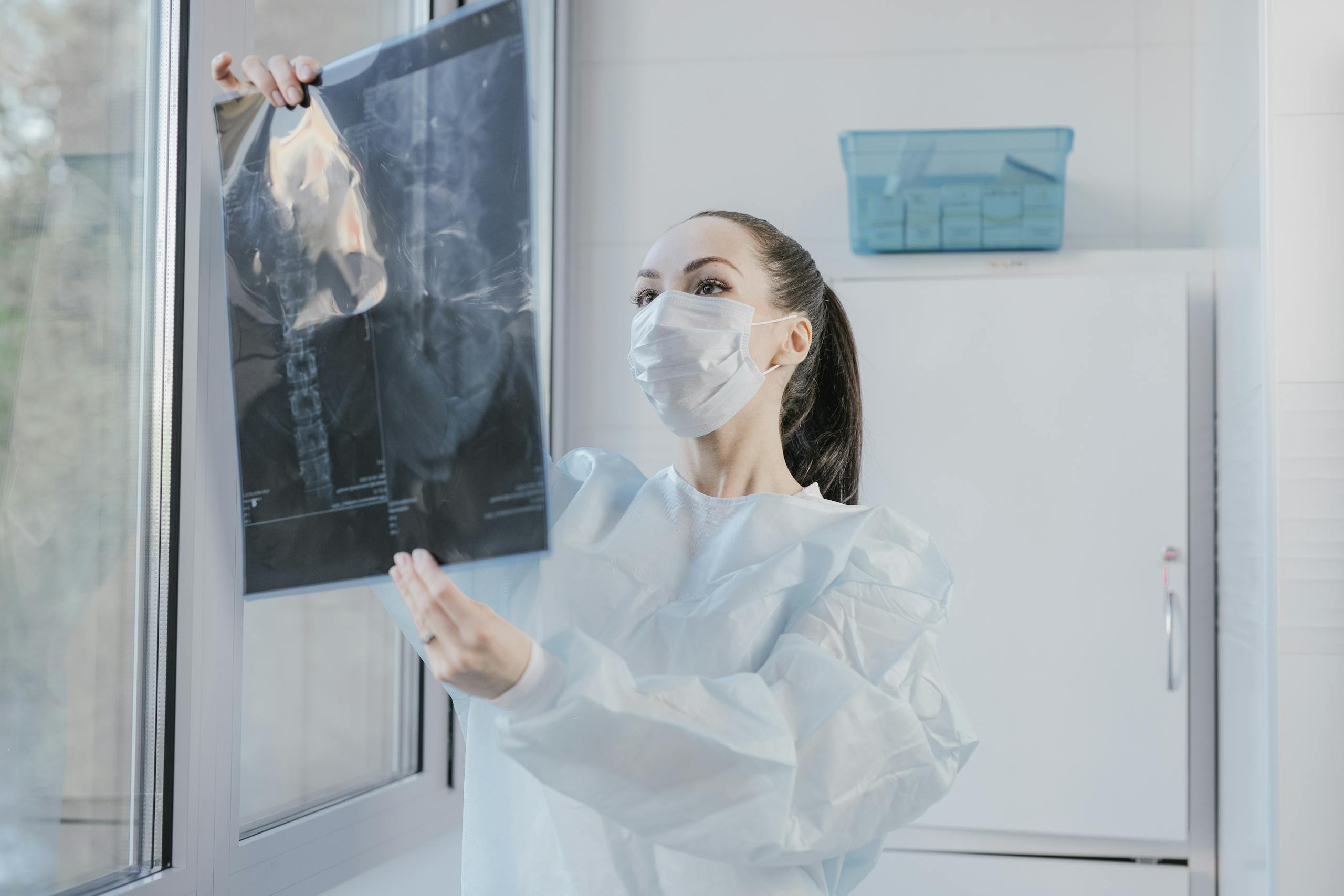 A medical professional examining an X-ray near a window in a clinical setting.